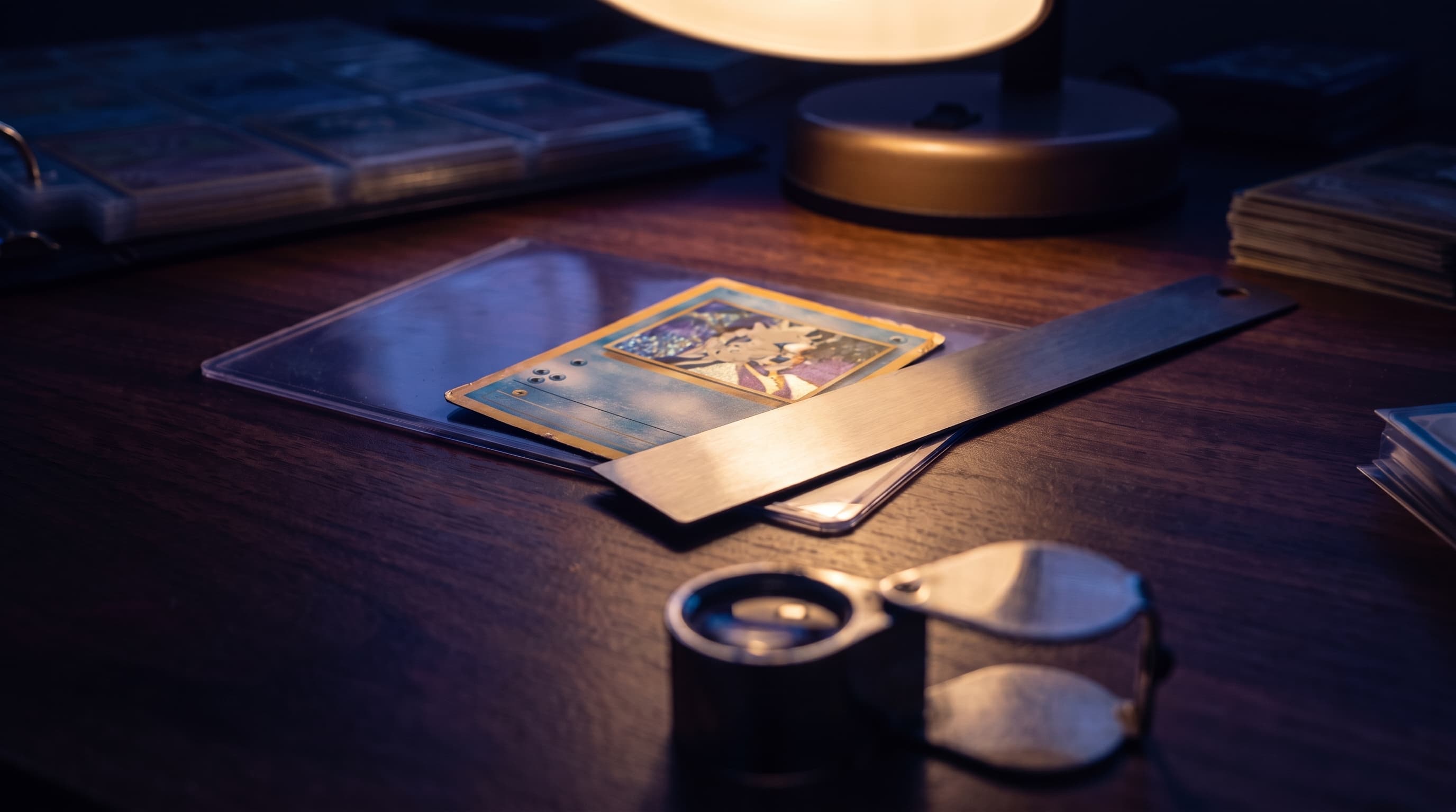 A ruler laid across the lower border of a vintage trading card on a lamp-lit desk, with a loupe resting nearby in soft shadow.