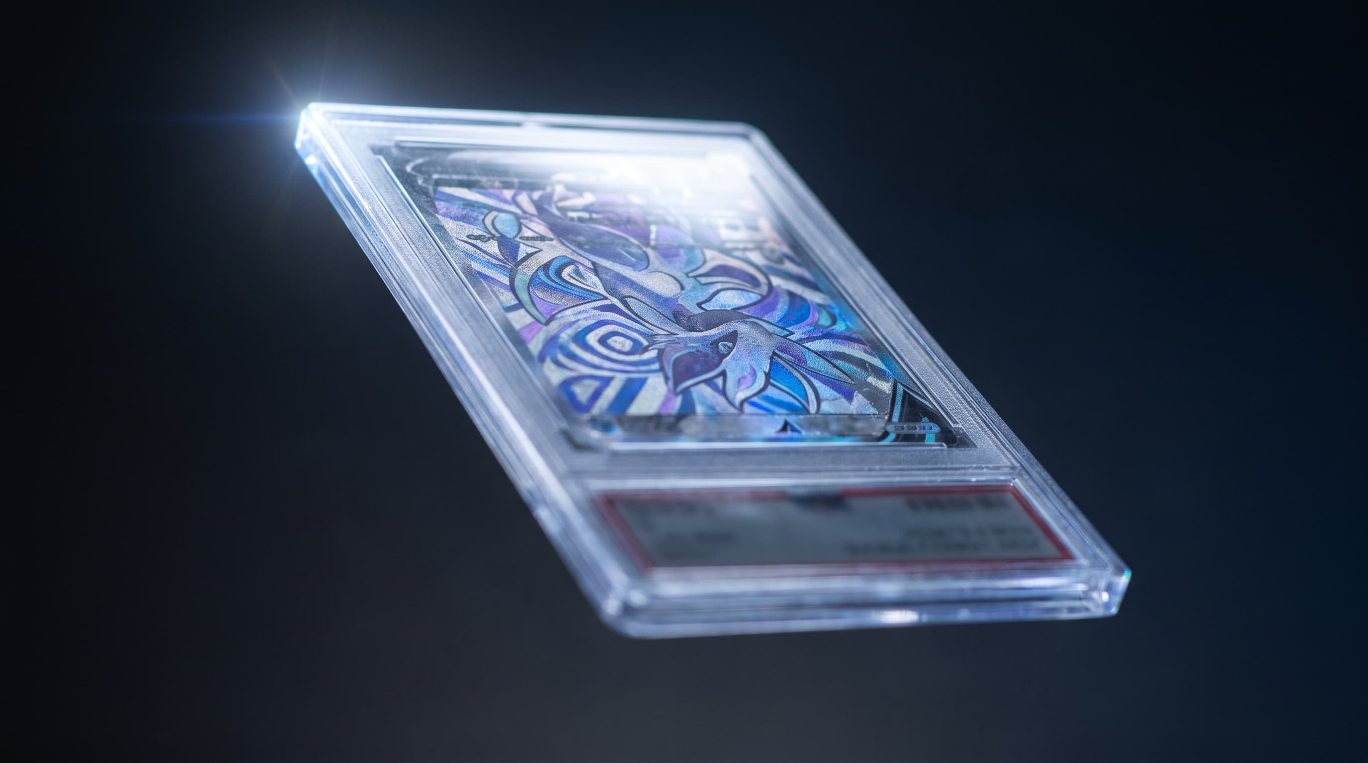 A single graded trading-card slab floats against a dark charcoal background, rim-lit along one edge, its abstract foil-patterned face catching cool light while the label strip beneath it stays softly out of focus.