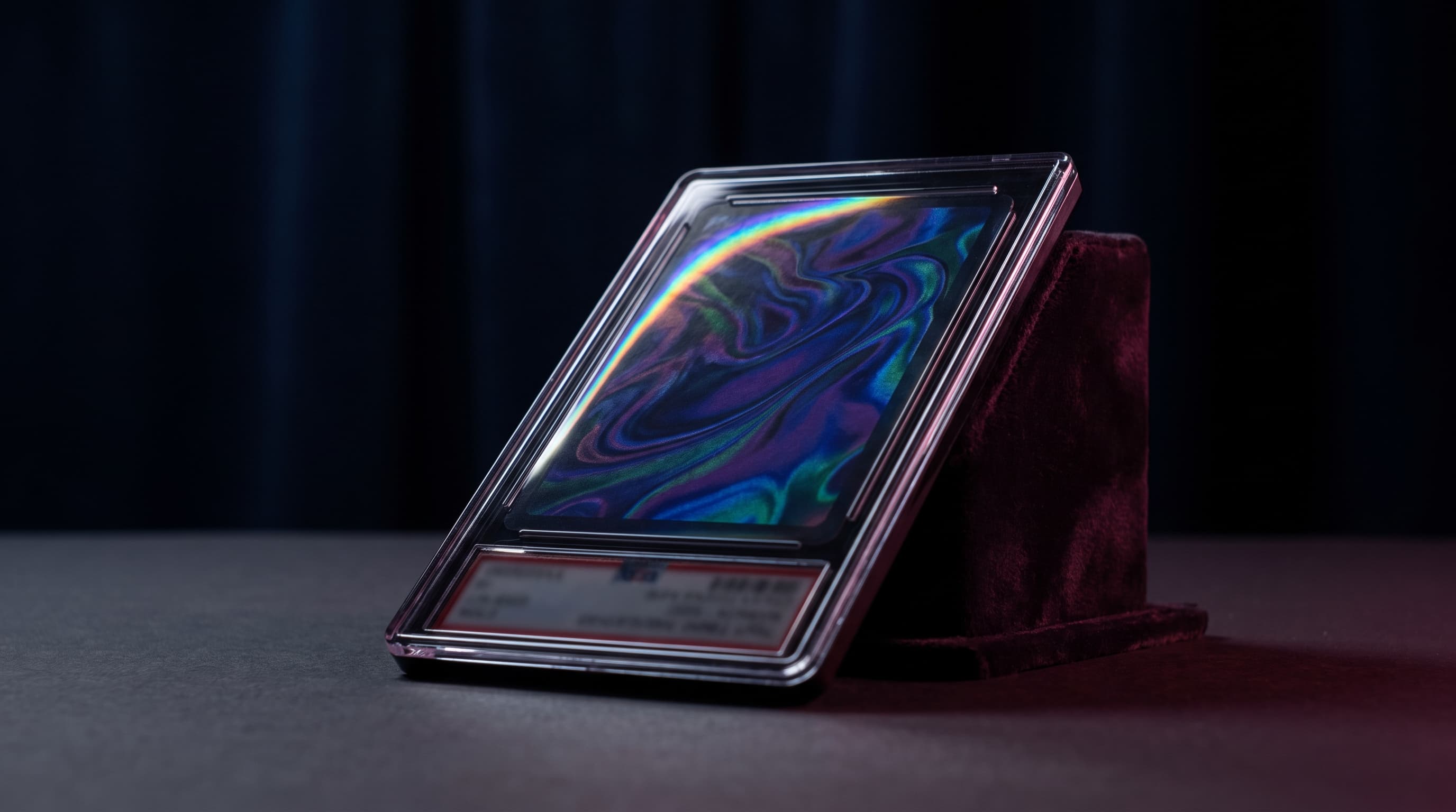 A single graded trading card slab lit dramatically against a dark background, its foil surface catching a thin rainbow-colored glare along one edge